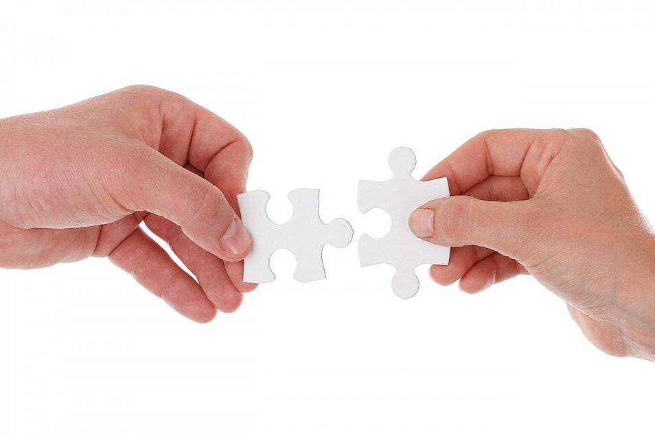 Zwei Hände halten je ein Puzzleteil, das zueinander gehört