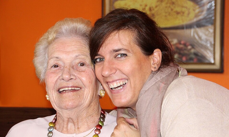 Freiwillige engagierte Frau Wange an Wange mit einer lachenden Seniorin