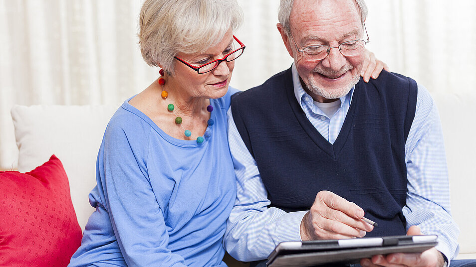 Seniorenpaar auf Sofa über Tablet gebeugt