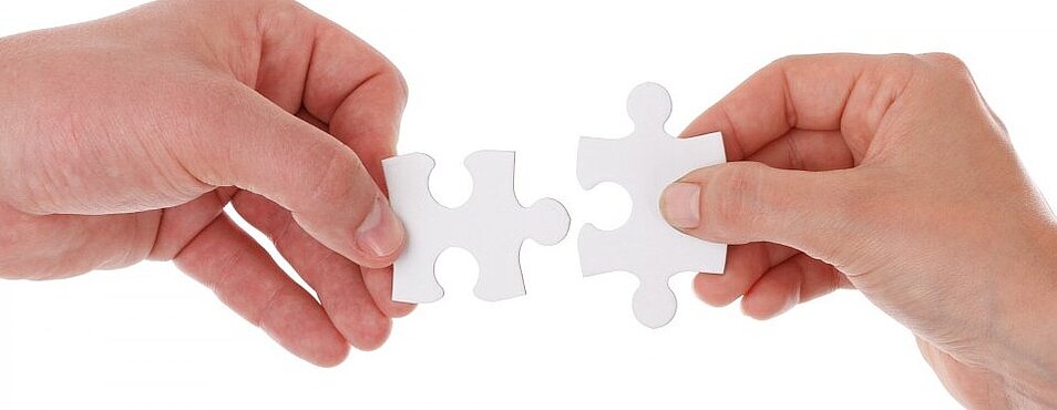 Zwei Hände halten je ein Puzzleteil, das zueinander gehört